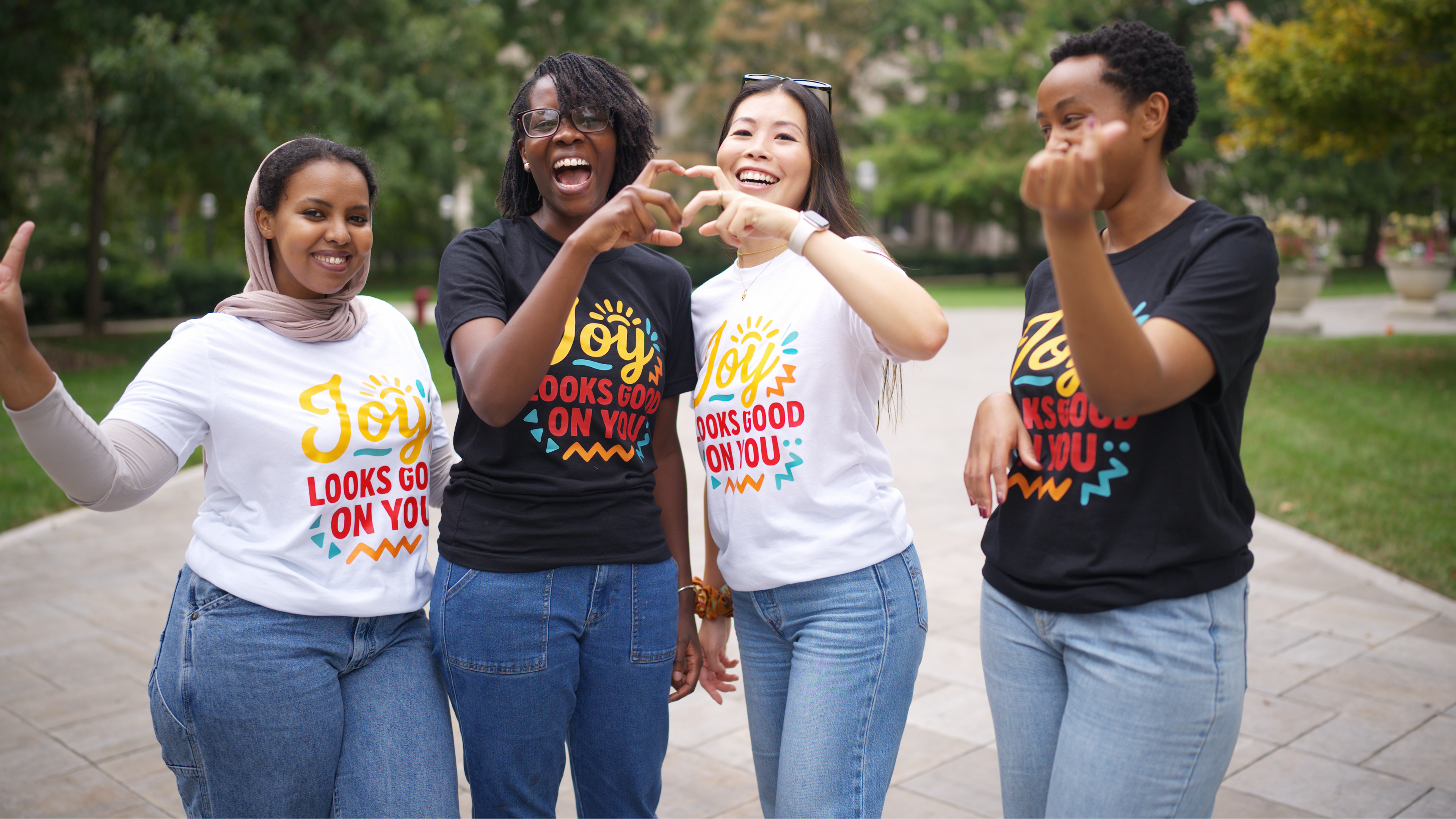 Four women wearing t-shirts with colorful designs outdoors.